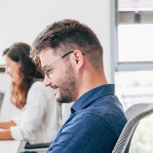 Un jeune homme du pole juridique sourit devant son ordinateur. On aperçoit sa collègue en arrière plan.