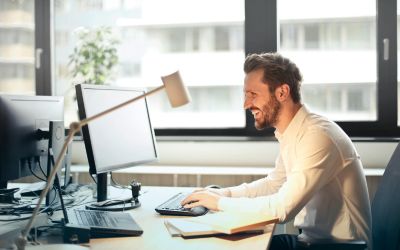 Un homme souriant travaillant sur un ordinateur dans un bureau moderne.