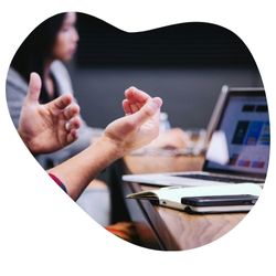 Gros plan sur des mains en train de gesticuler pendant une discussion, avec un ordinateur portable affichant un graphique