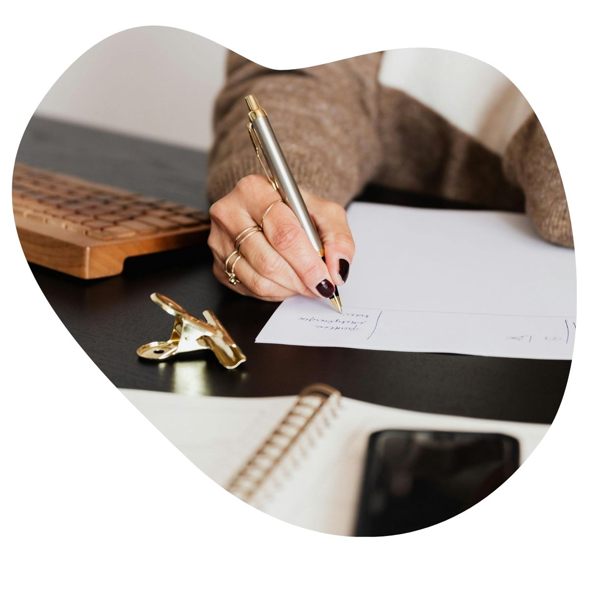 Gros plan sur une main en train d'écrire ou de signer un document, avec un stylo et un carnet.