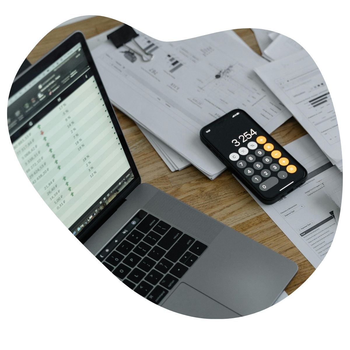 Un ordinateur portable affichant des données financières et un smartphone en mode calculatrice posé sur des documents papiers.